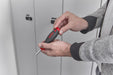 Person using a red and black screwdriver on a white cabinet.