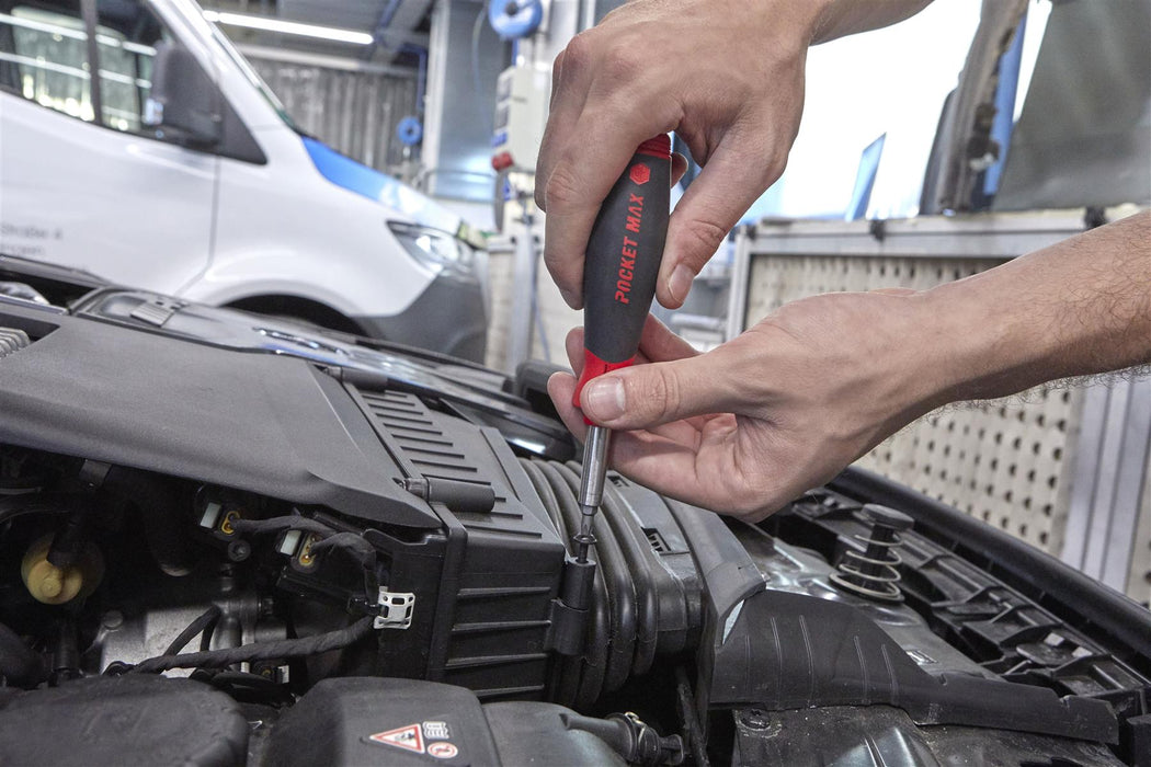 Person using a screwdriver to work on a car engine with a blurred background
